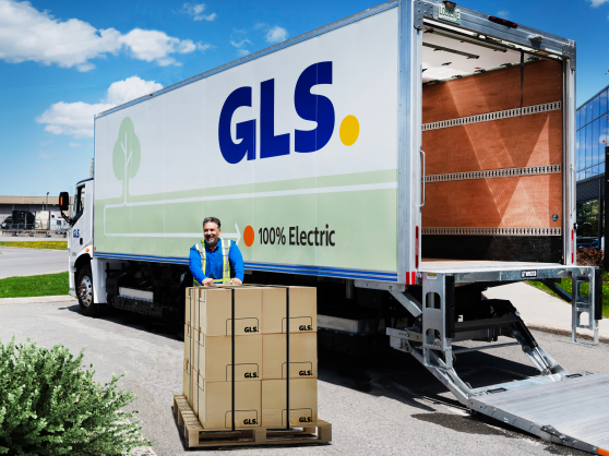 A driver delivering a pallet of boxes standing next to a 100% electric GLS truck.