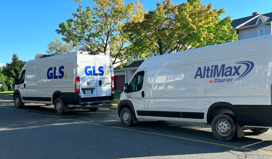 A GLS parcel van followed by an AltiMax Courier parcel van driving down a residential street.