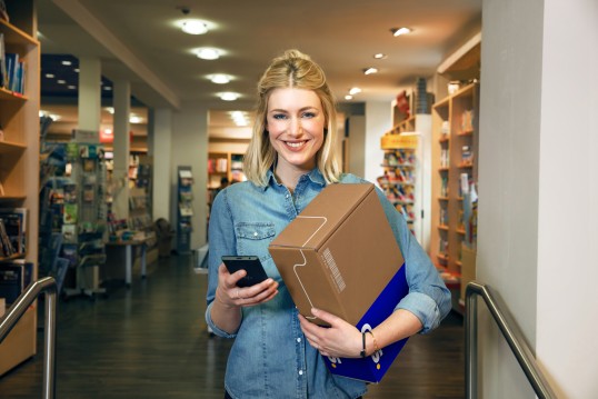 Femme blonde souriante tenant un colis dans un magasin.