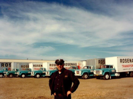 Man standing in front of Rosenau trucks in the yard in the 1950's