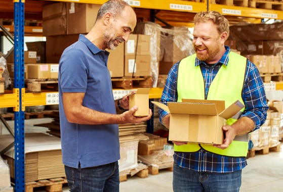 Two men in a warehouse holding small boxes