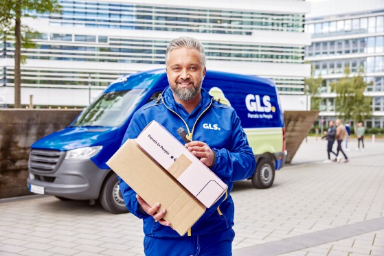 GLS driver holding two parcels on his hands and behind there is GLS electric van